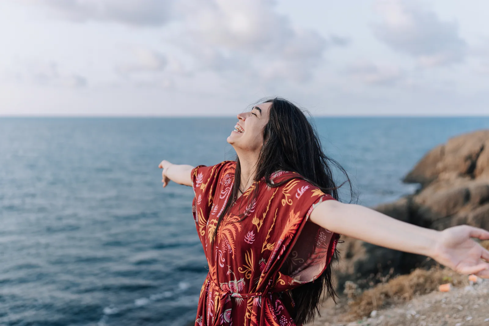 Woman standing by the ocean with her arms outstretched